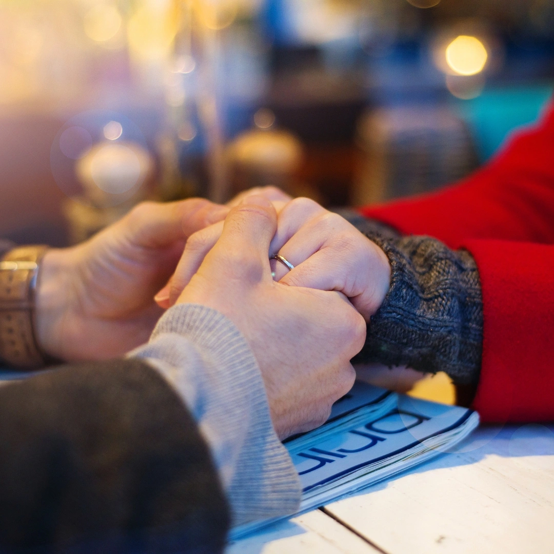 Hände eines Mannes halten die Hände einer Frau am Tisch