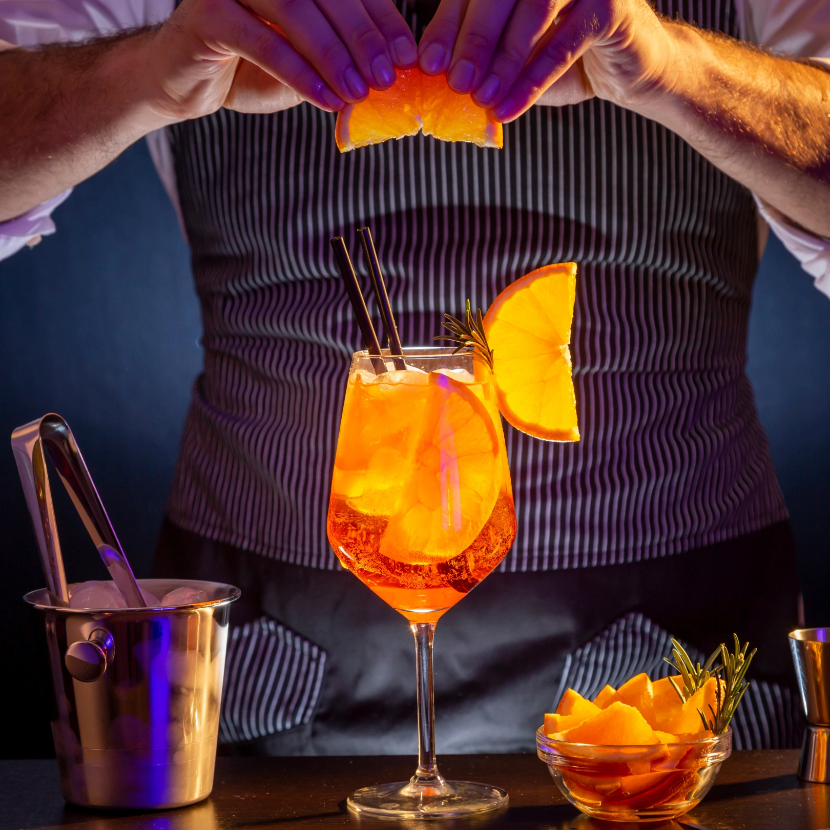 Bartender with a slice of orange in his hand above a cocktail with oranges inside