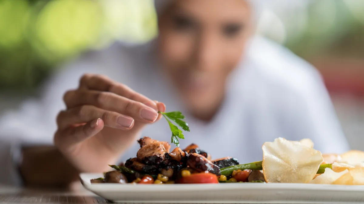 Hand legt Petersilie auf stilvoll hergerichtetes Essen