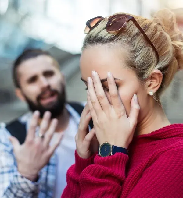 woman is holding her hands in front of her face man in the background